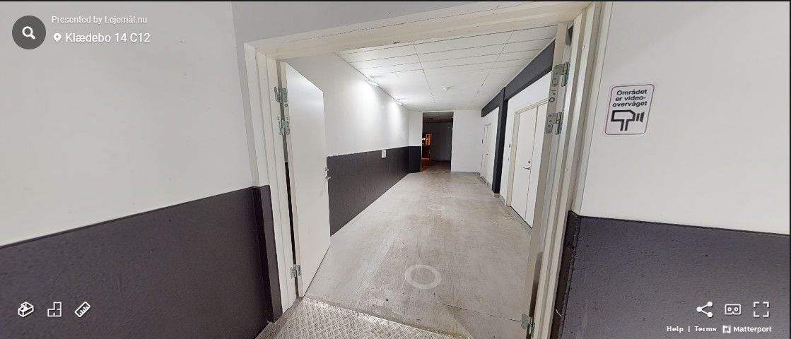 Lang, tom gang i et erhvervscenter med hvide og sorte vægge og to døre til siderne