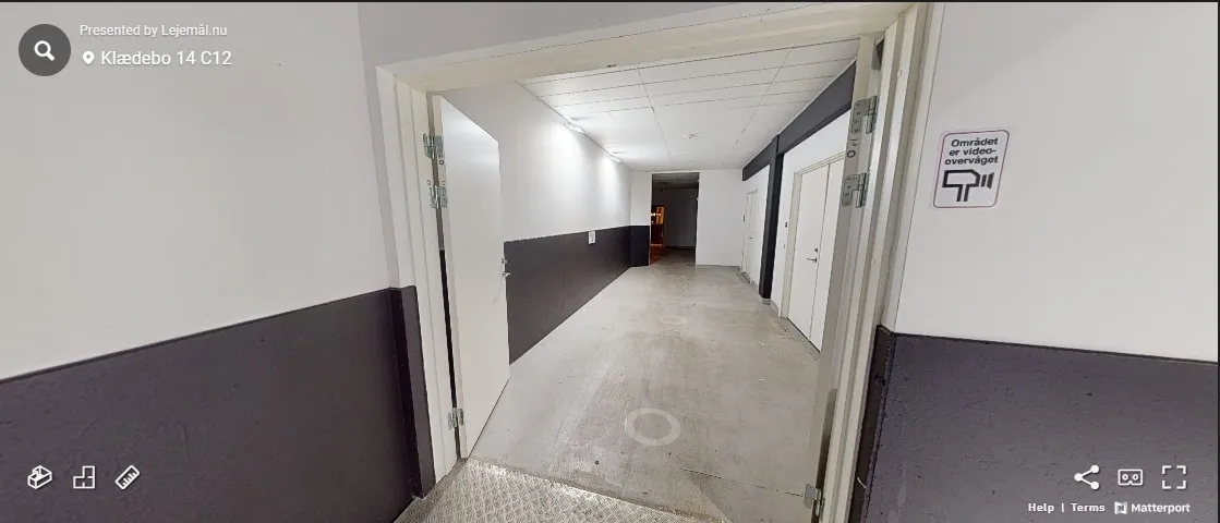 Lang, tom gang i et erhvervscenter med hvide og sorte vægge og to døre til siderne