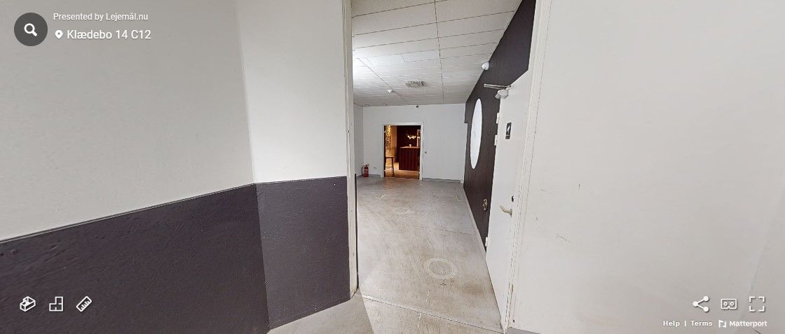 En mørk og lys hal med gulv og vægge samt udgangsdør, der er åben og leder ind i en lille stue.