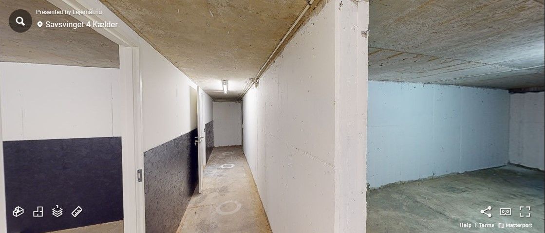 Hallen med hvide vægge og cementgulve og to åbne døre med et lys i bunden af korridoren