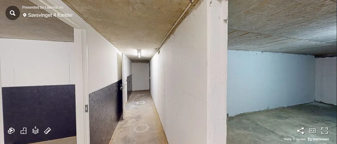 Hallen med hvide vægge og cementgulve og to åbne døre med et lys i bunden af korridoren