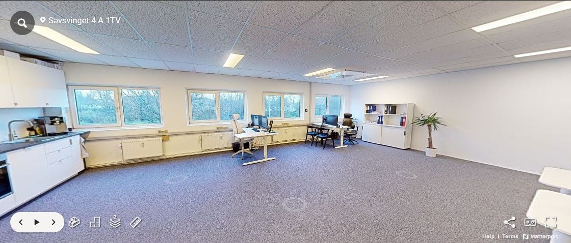 Røgsuger over køkken med moderne hvide skabsfronter og en hvid skrivebord. Gulvet er dækket med blødt gråt gulvtæppe og der