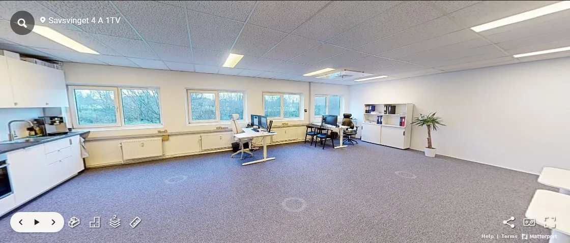 Røgsuger over køkken med moderne hvide skabsfronter og en hvid skrivebord. Gulvet er dækket med blødt gråt gulvtæppe og der