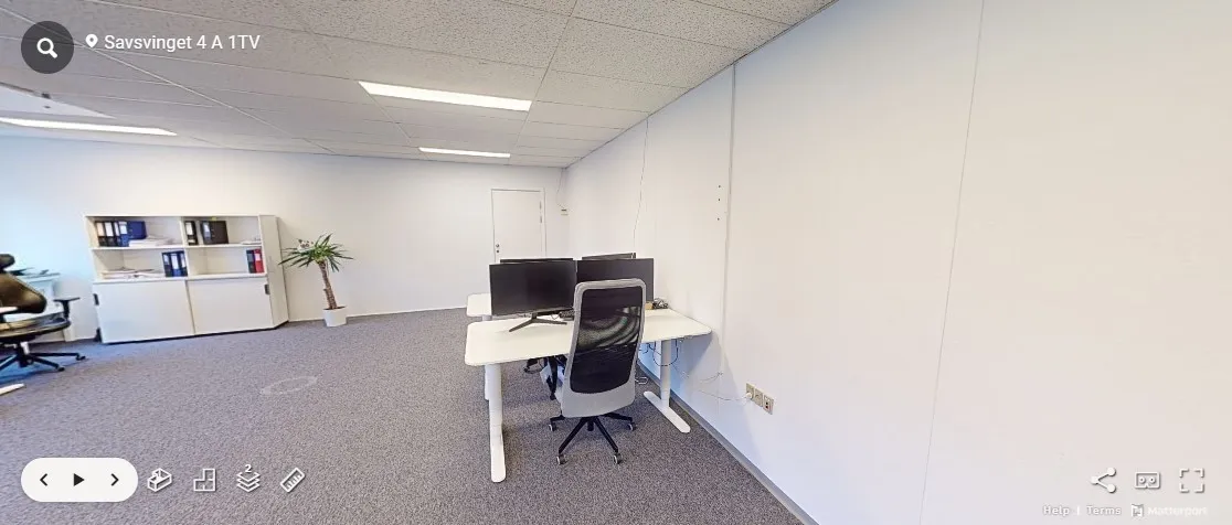 Et tomt kontor med et hvidt bord og en høj, hvid hylde med bøger og en lille plante i en gryde