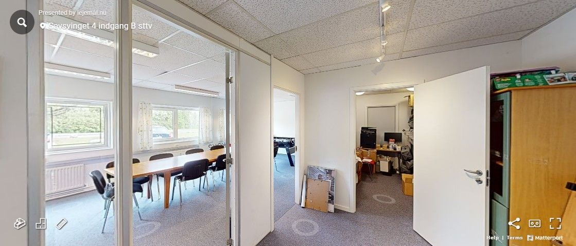 En tom kontorlokal med bord og stole samt en åben dør og træskab med ting på.