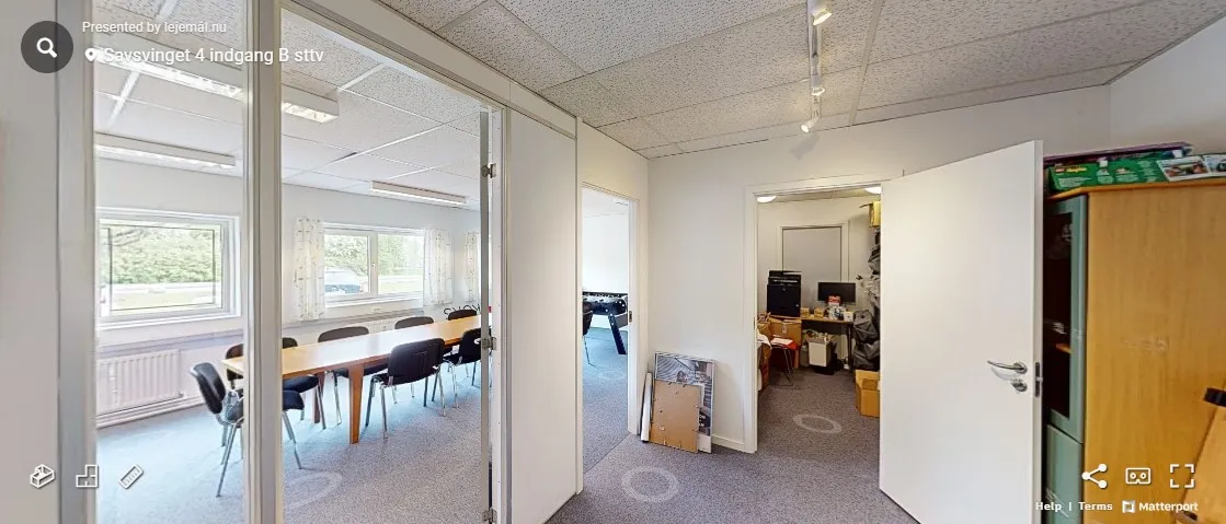 En tom kontorlokal med bord og stole samt en åben dør og træskab med ting på.