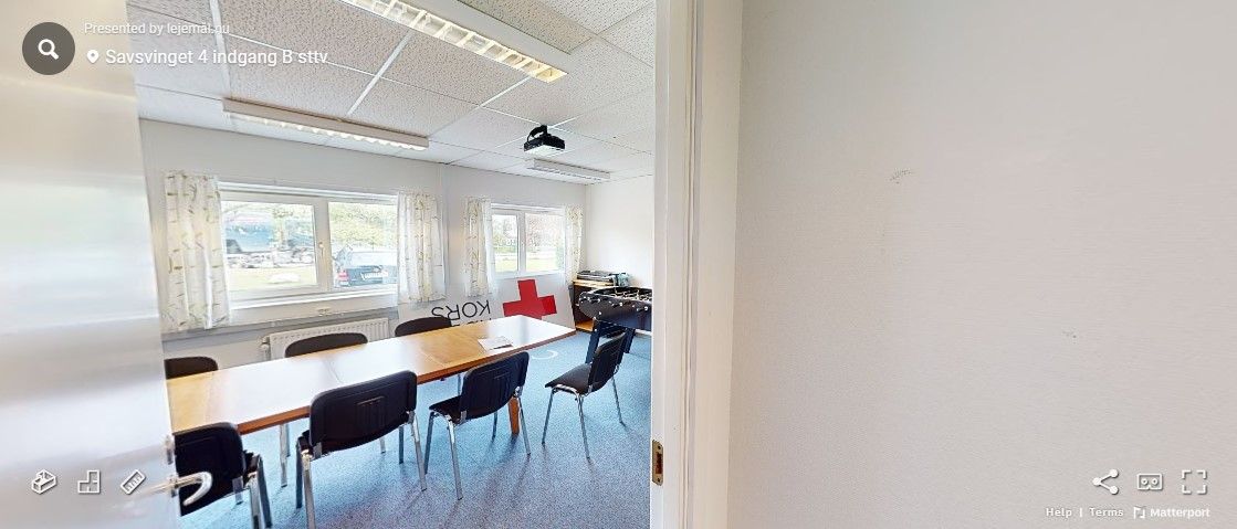 Et rum med en lang bord, flere stole, en projektor og et rødt kors på væggen