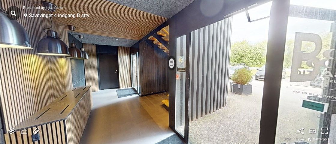 Savsvinget 4 i Hørsholm har en elegant, træbeklædt væg og en glasdør med reklame. Der er en stigning med trætrin og en vej