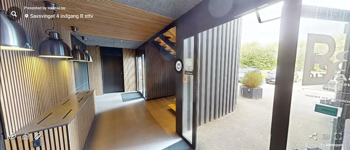 Savsvinget 4 i Hørsholm har en elegant, træbeklædt væg og en glasdør med reklame. Der er en stigning med trætrin og en vej