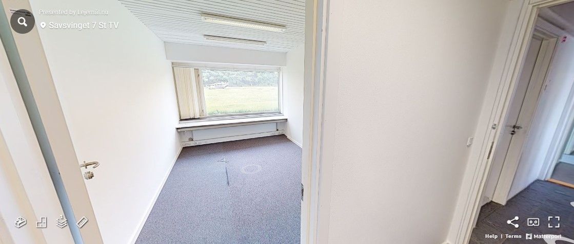 En tom kontorlokal i Savsvinget 7 med lyse loftslampe, hvidt panel og gulvbelægning og et stort vindue med udsigt til en