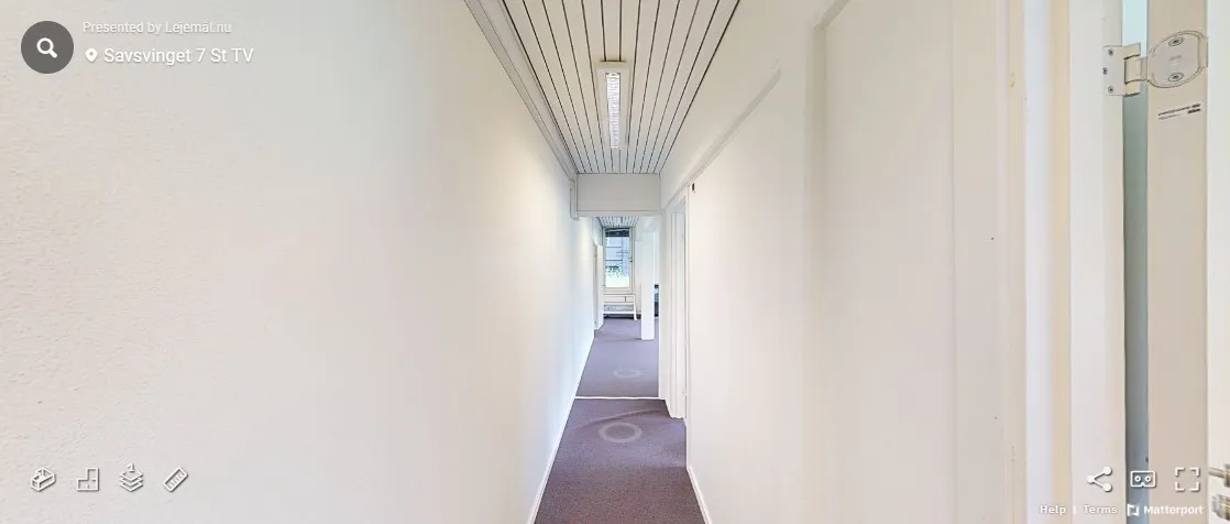 En tom korridor med hvide vægge og en rød gulvbelægning og søjler med lys.