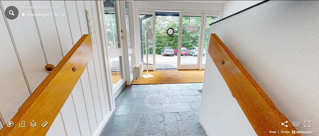 Foto af et hus med indgangsdør og to træhåndtag. Der er et gulvbelæg og en dørmåtte i gulvet. Der er et søjlesystem, og der