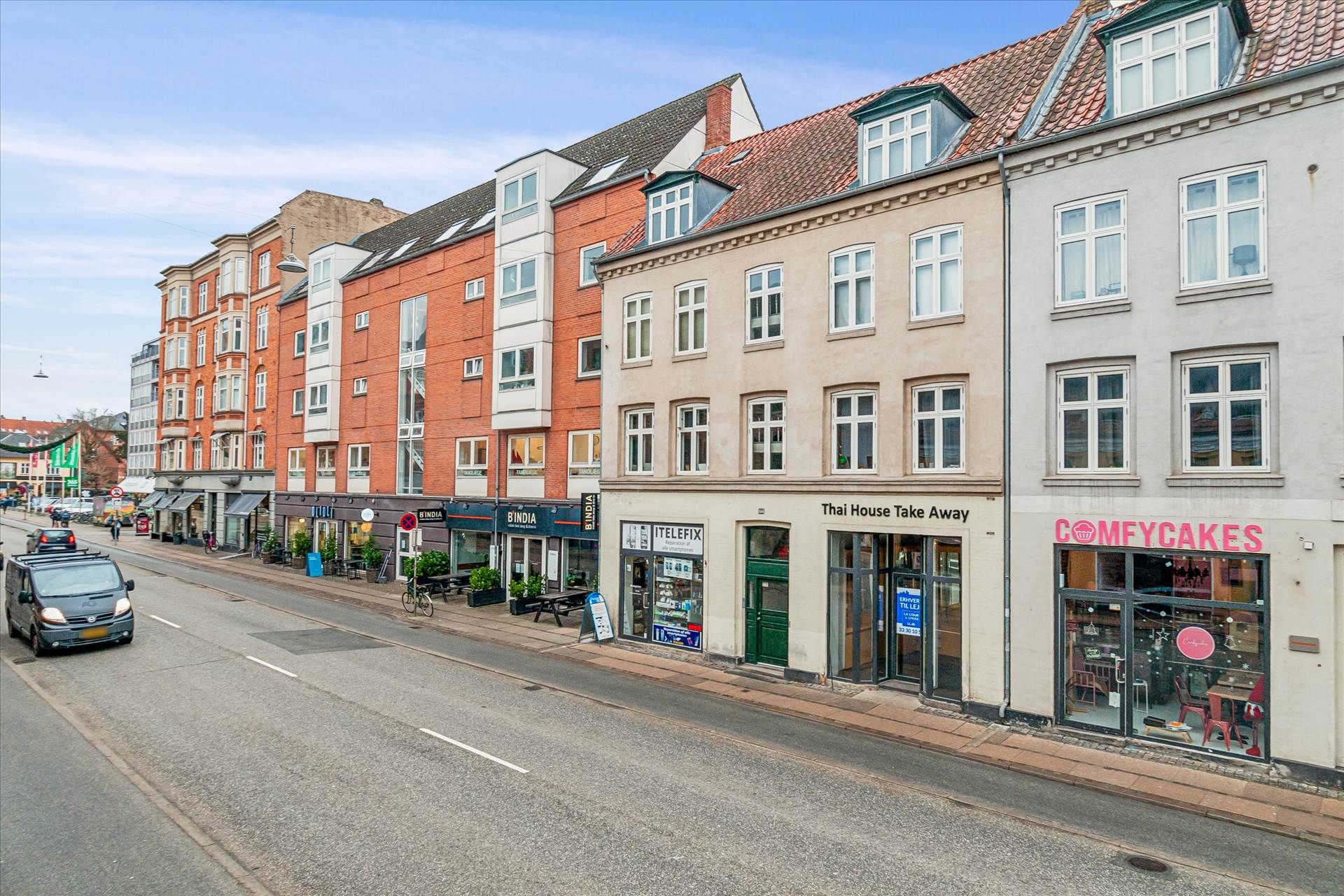 Butiksfronter med forretninger og restauranter på Amagerbrogade i København og en kørende bil