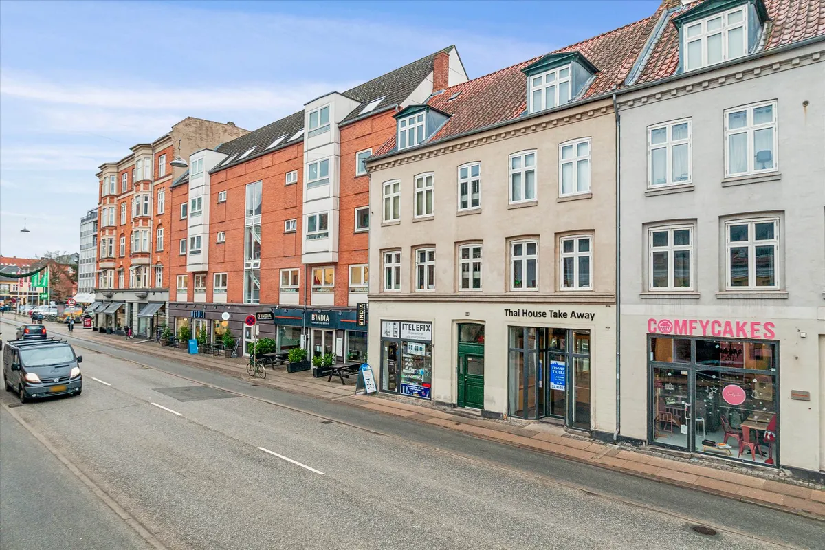 Butiksfronter med forretninger og restauranter på Amagerbrogade i København og en kørende bil