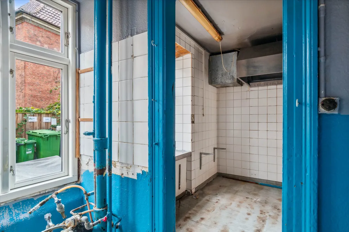 Køkken med blå døre og røde gulve, hvor der er et vindue og røret til vand og gas