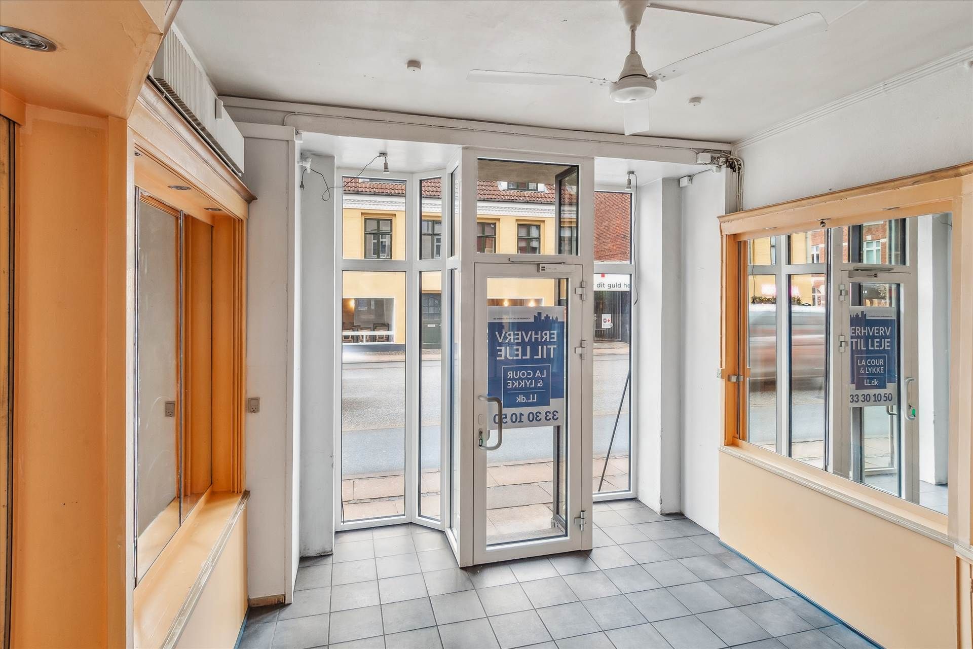 Åben dør til en lille butik med glasruder og tekst på døren om åbningstider og kontaktoplysninger