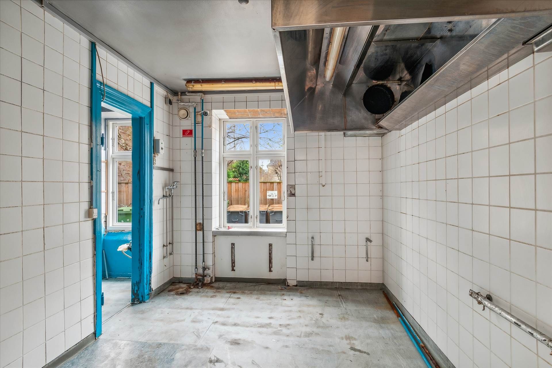 Røgskade på loftet i køkken med to vinduer og lyserøde døre, samt højt monteret ventilationsskakt