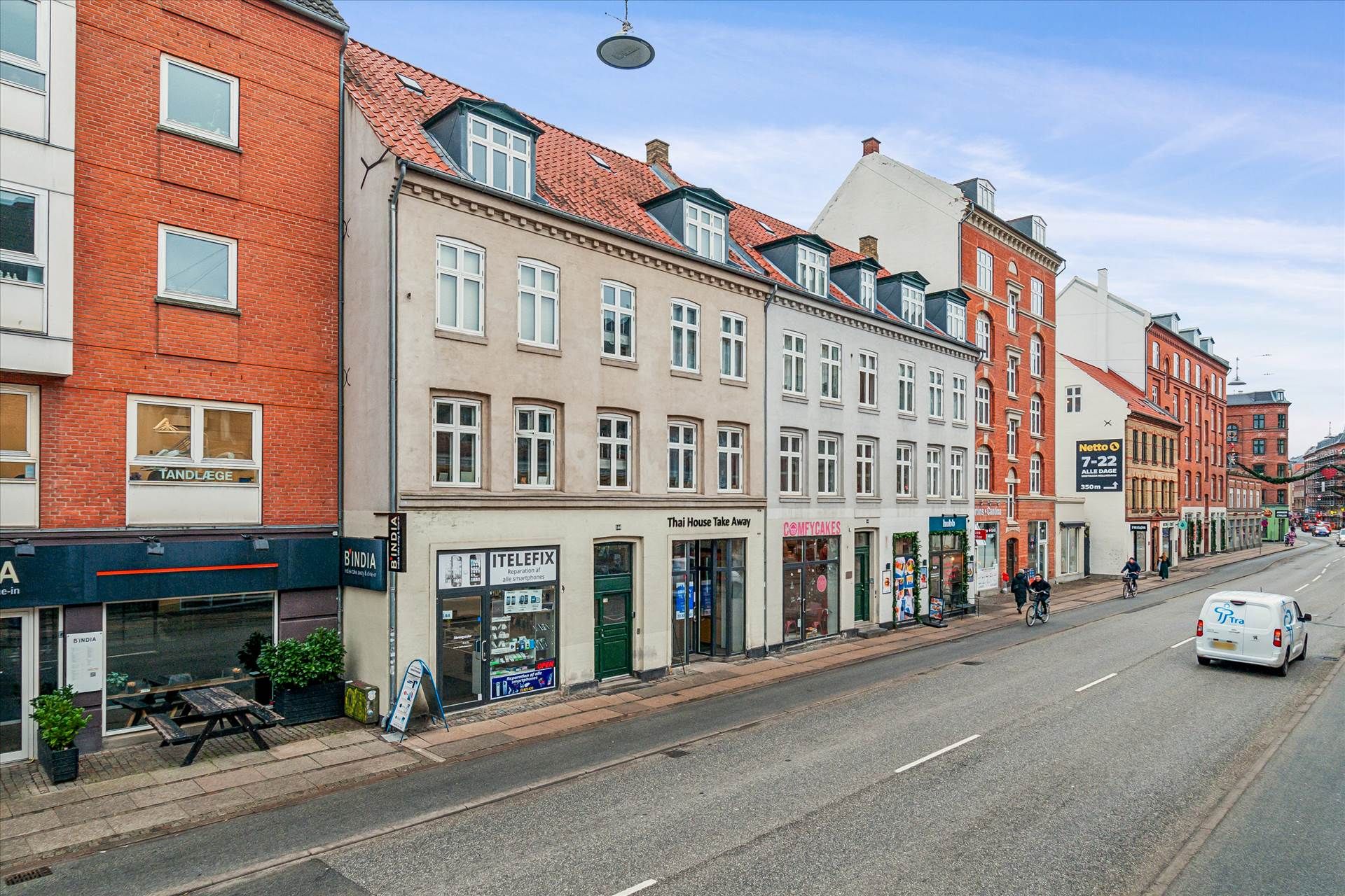 Butikkerne er placeret på Amagerbrogade, hvor der er en hvid lastbil, der kører, og folk går forbi