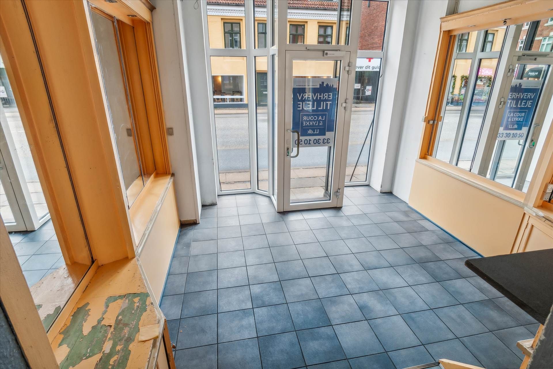 Lejlighed med indgangsdør og gulv i blå tøjler og gulvpaneler i hjørnet og tekst om udlejning