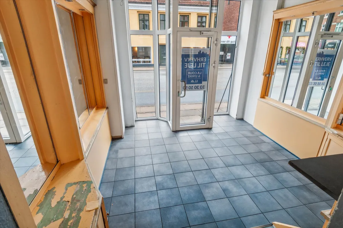 Lejlighed med indgangsdør og gulv i blå tøjler og gulvpaneler i hjørnet og tekst om udlejning