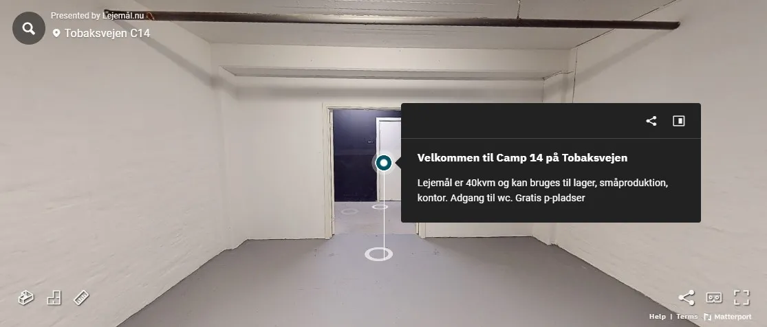 En tom gang med hvide vægge og cementgulve. Der er en dør til venstre og en tekst med oplysninger om ejendommen til højre.