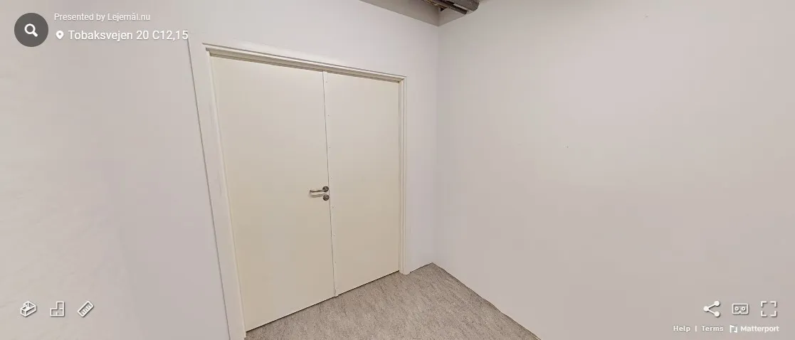 Tomt rum med hvide vægge og gulvtæppe samt hvide døre med håndtag og metalbeslag.