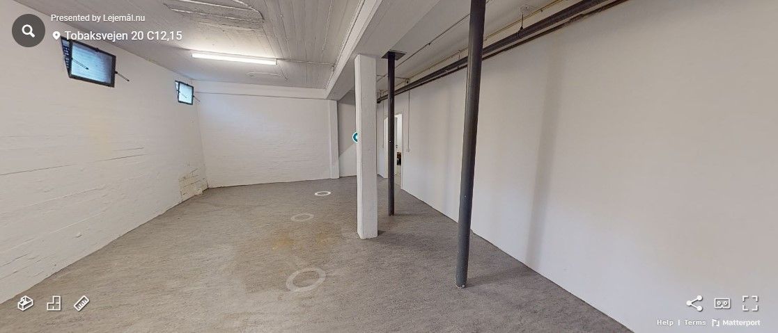 Ledig lagerlokale i Tobaksvejen med to mindre vinduer og to søjler, der står på en betongulv