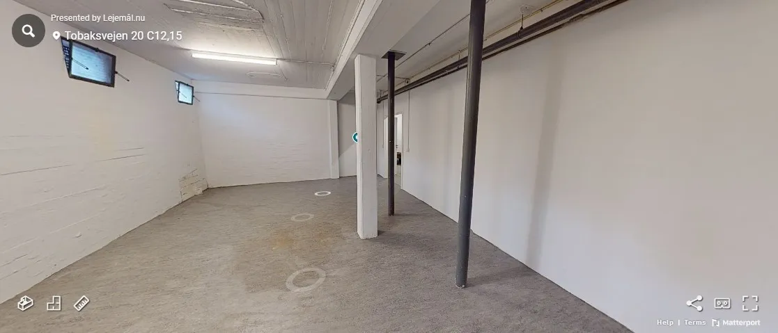 Ledig lagerlokale i Tobaksvejen med to mindre vinduer og to søjler, der står på en betongulv