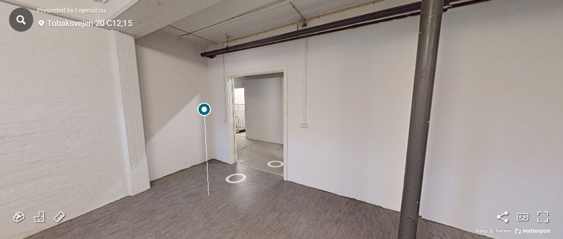 En tom lokale med hvide vægge og gulv med trægulv. Der er en dør, der er åben. Der er et tekstfelt med adressen Tobaksvejen