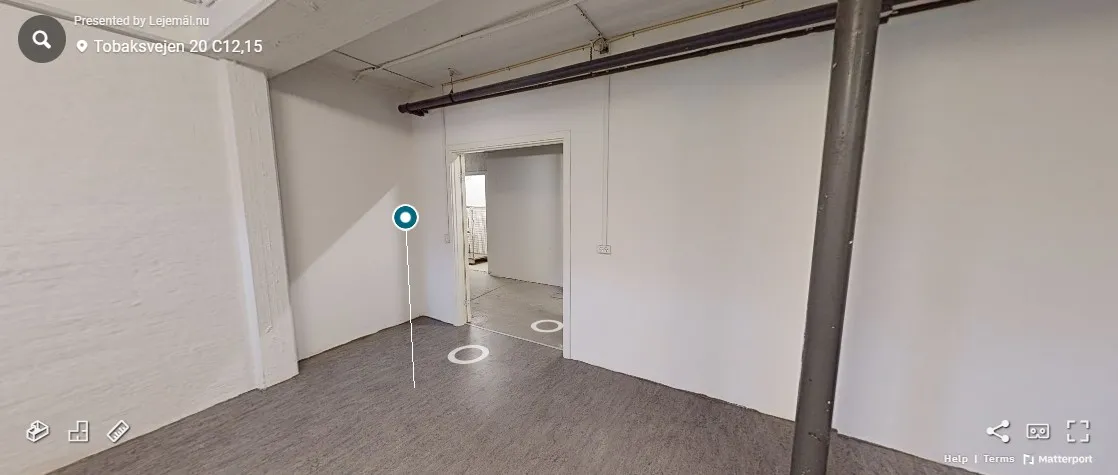 En tom lokale med hvide vægge og gulv med trægulv. Der er en dør, der er åben. Der er et tekstfelt med adressen Tobaksvejen