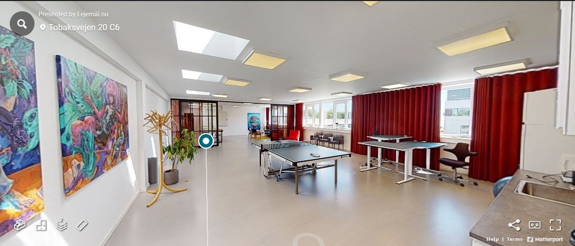 Godt lyst kontor med lyse lofter og store vinduer, indretning med moderne møbler og kunstværker samt rekreativt område med