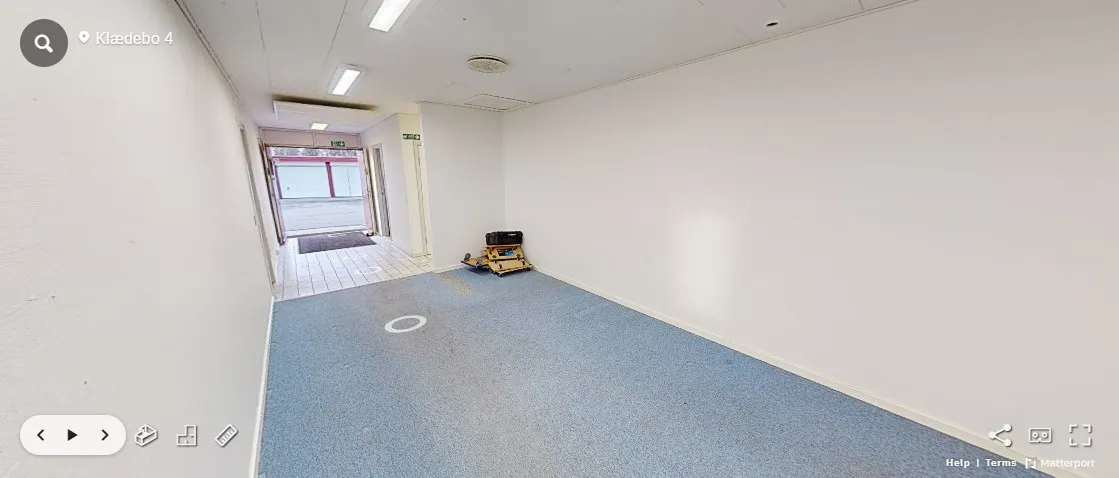 Tomt lokale med hvide vægge og blå gulvbelægning, en gulvoplister og et åbent dørkar i midten af rummet