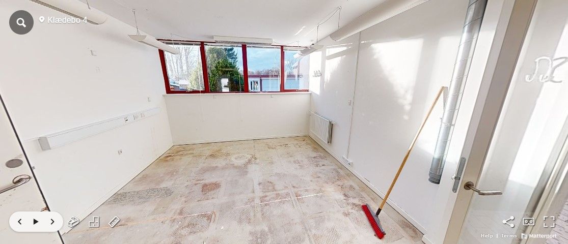 Ledig kontorlokaler med vindue og radiator i Hørsholm, udstyret med renserstang og to lysekroner, der er ophængt på loftet.