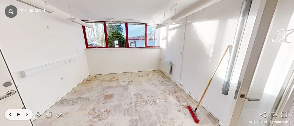 Ledig kontorlokaler med vindue og radiator i Hørsholm, udstyret med renserstang og to lysekroner, der er ophængt på loftet.