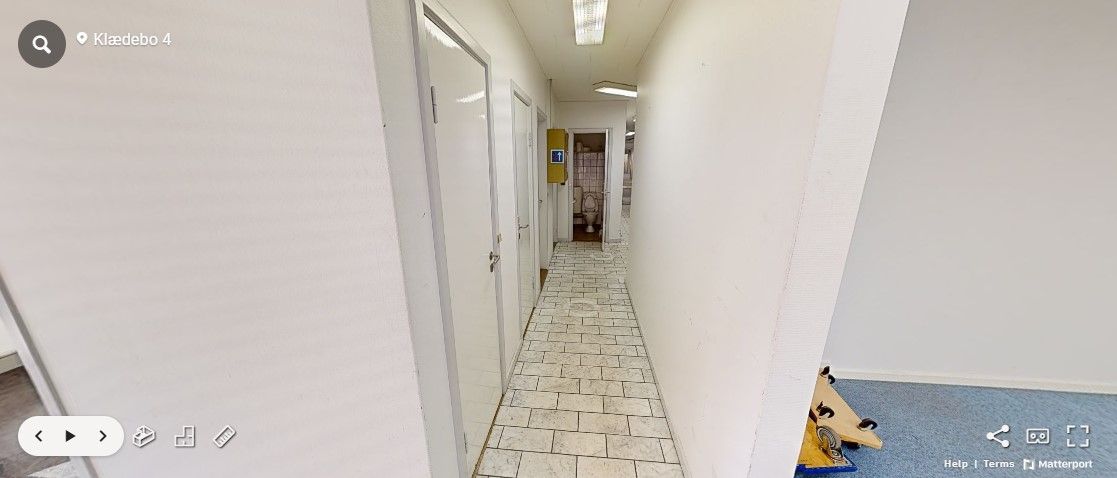 Hvid, fladt loft med to lyskilder og en toiletdør. En tom gang med klinkergulv og hvide vægge. En toilet, hvor der er en gul