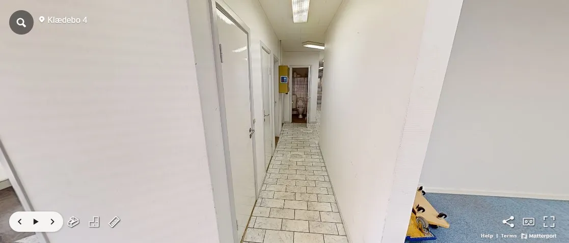 Hvid, fladt loft med to lyskilder og en toiletdør. En tom gang med klinkergulv og hvide vægge. En toilet, hvor der er en gul