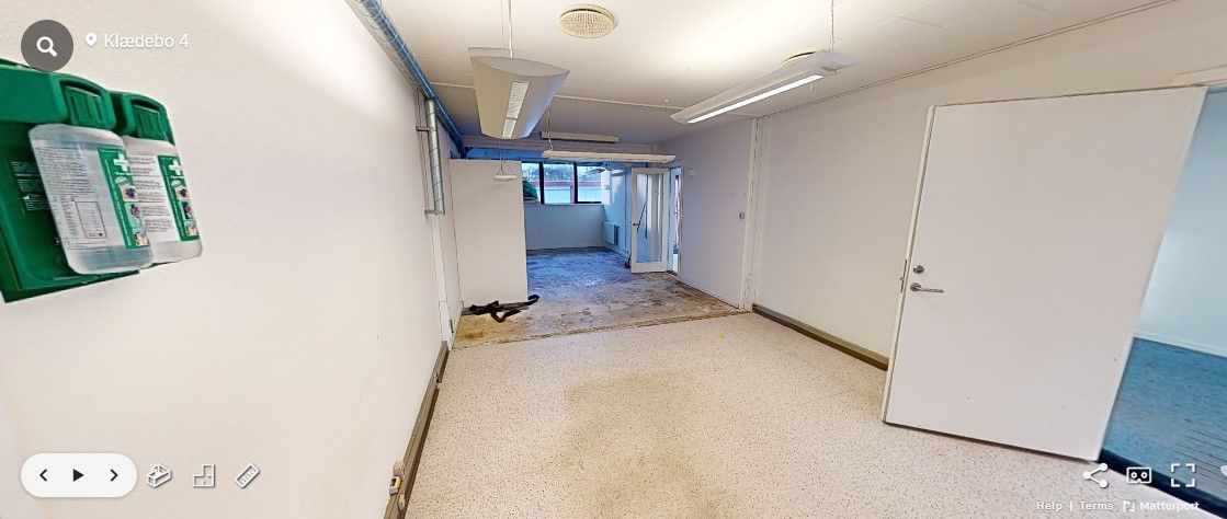 Kontor med moderne design og lyse loftslamper. To døre med håndtag og et glasvindue. En grøn søjle med flasker til