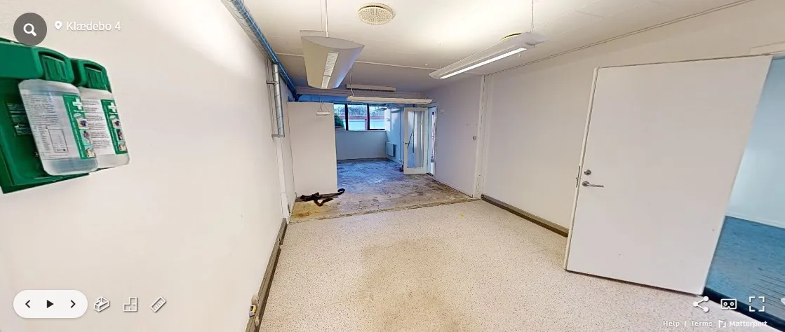 Kontor med moderne design og lyse loftslamper. To døre med håndtag og et glasvindue. En grøn søjle med flasker til