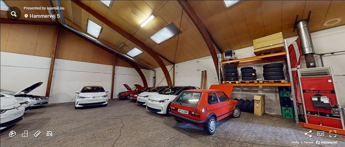 Garage med forskellige biler, herunder en rødt kabinet med nummerplade 52-59-88, flere hvide biler og lagerhylder med dæk.