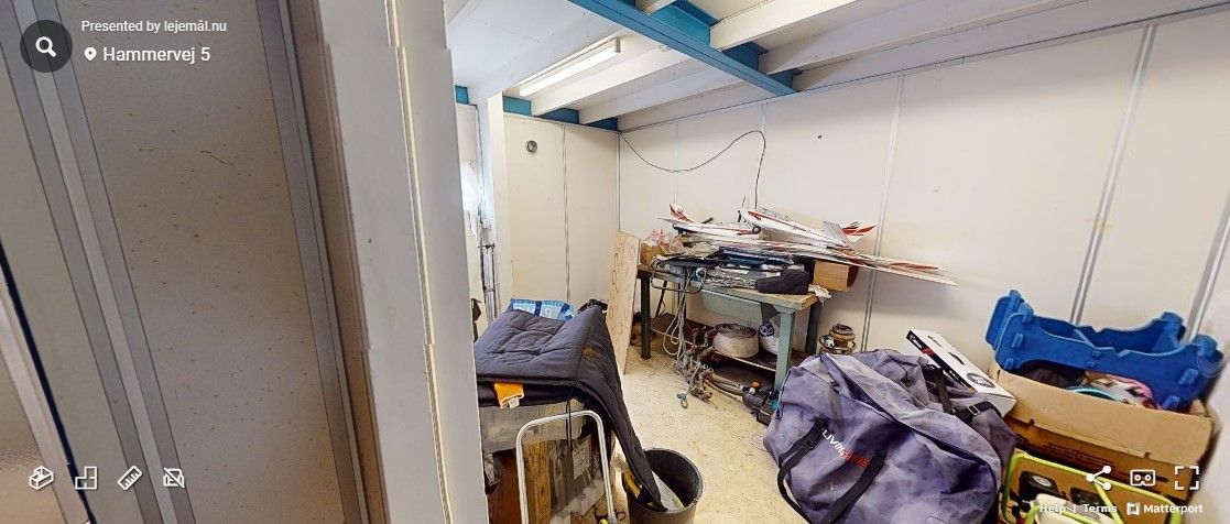 Flymodeller og diverse ting står i en lagerbygning. På gulvet ligger en pude, en bøsse og en papkasse. I midten er en