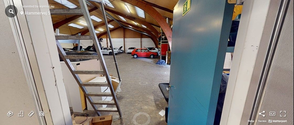 Garage med åbne døre og lager, to biler parkeret i baggrunden, og en redningsvej er markeret med et gult skilt