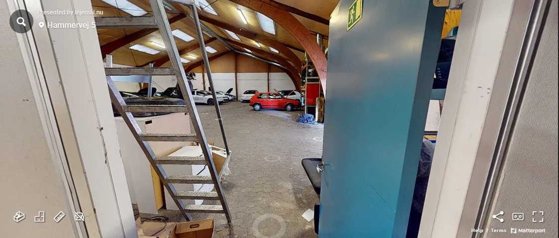 Garage med åbne døre og lager, to biler parkeret i baggrunden, og en redningsvej er markeret med et gult skilt