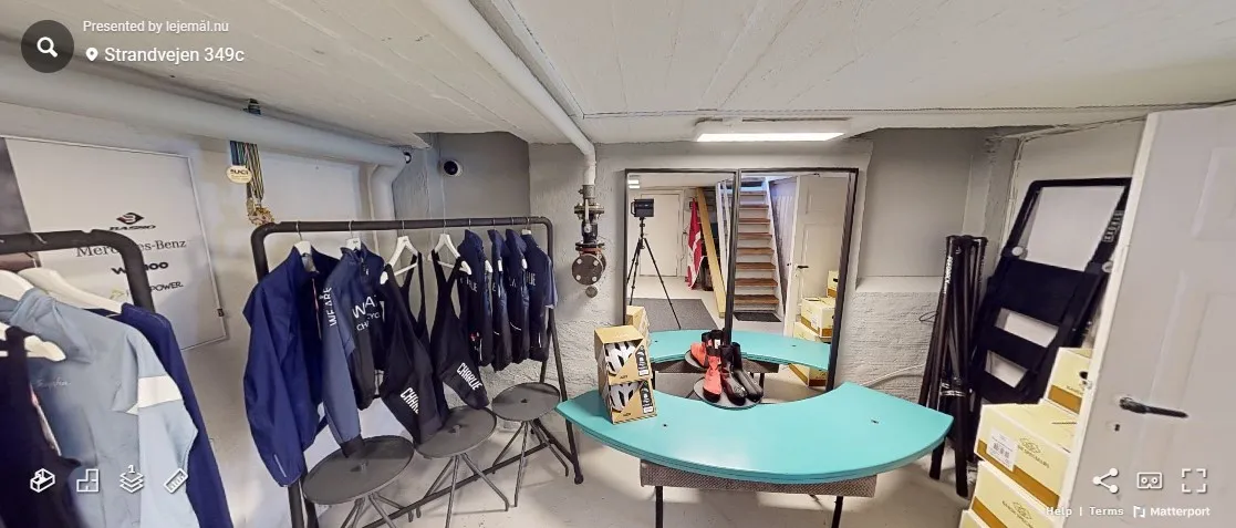 Klædeskab med hængegrej og tøj, hvid gulv, røde sko på gulvet, høj gulvlampe, hvid dør og trapper i baggrunden