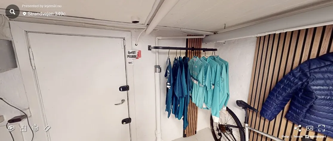 En hvid dør med skilte, der siger "Quiet Please" og WC. Klær er hængende på en kleshenger. Et cykelhjul og en blå jakke er