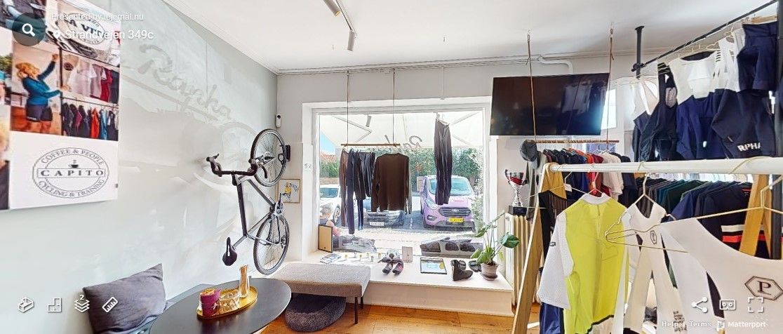 På indersiden af tøjbutik er der tøj hængende og opstillet. Der er også en stol og et bord med en søjle og en pude på bordet.