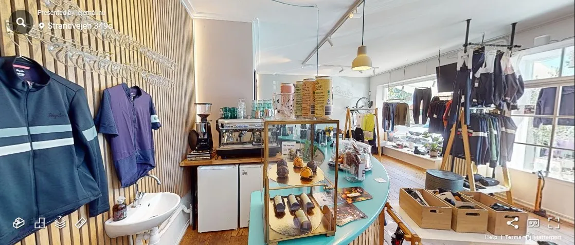 Tøj og cykeludstyr forhandleren med kaffemaskine og desserter i Klampenborg. Butikken har hvide vægge og lyse gulve.