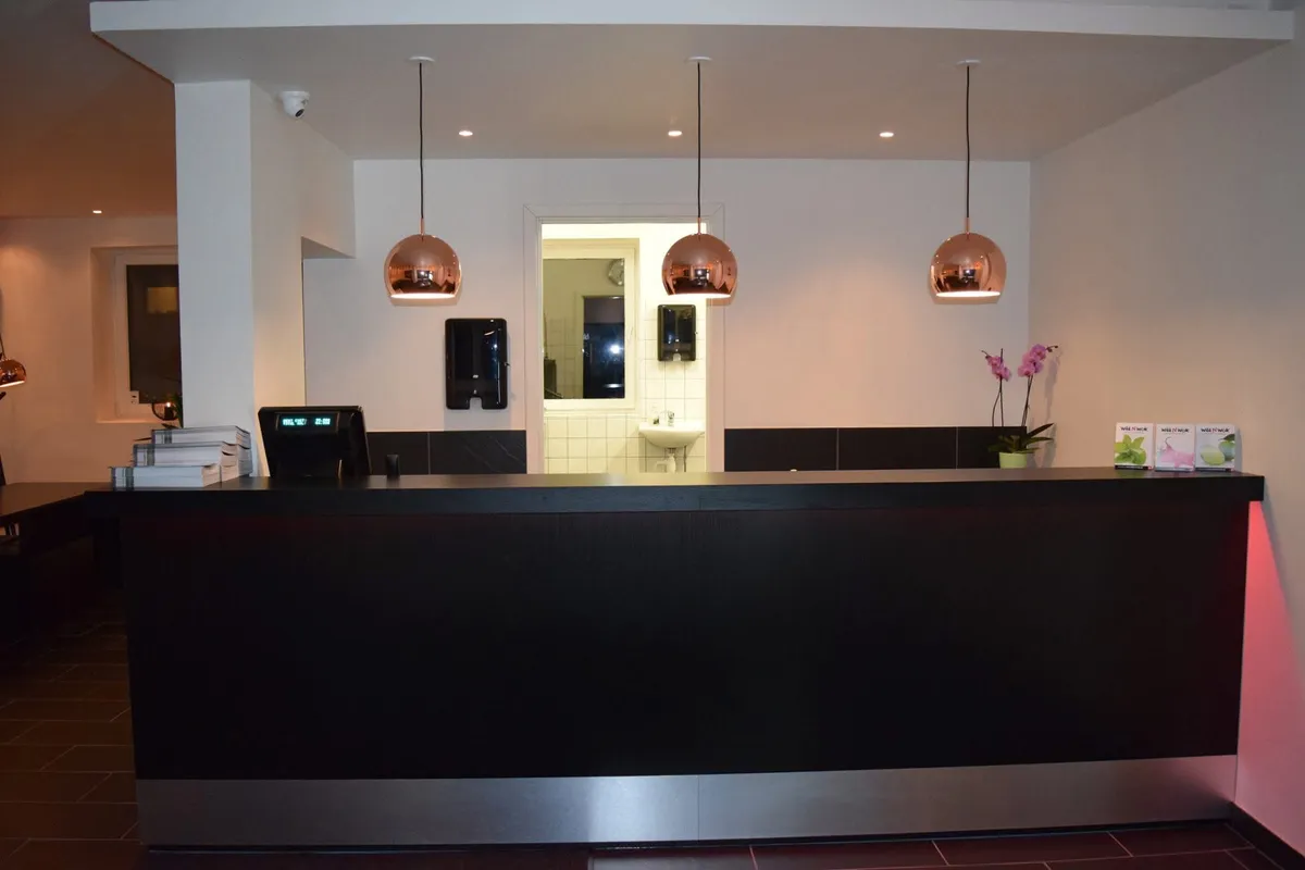 Sort og gulvmonteret salgssted med en blomst og 3 kobberkronleuchter. Et toilet med spejl og håndvask samt et skrivebord med