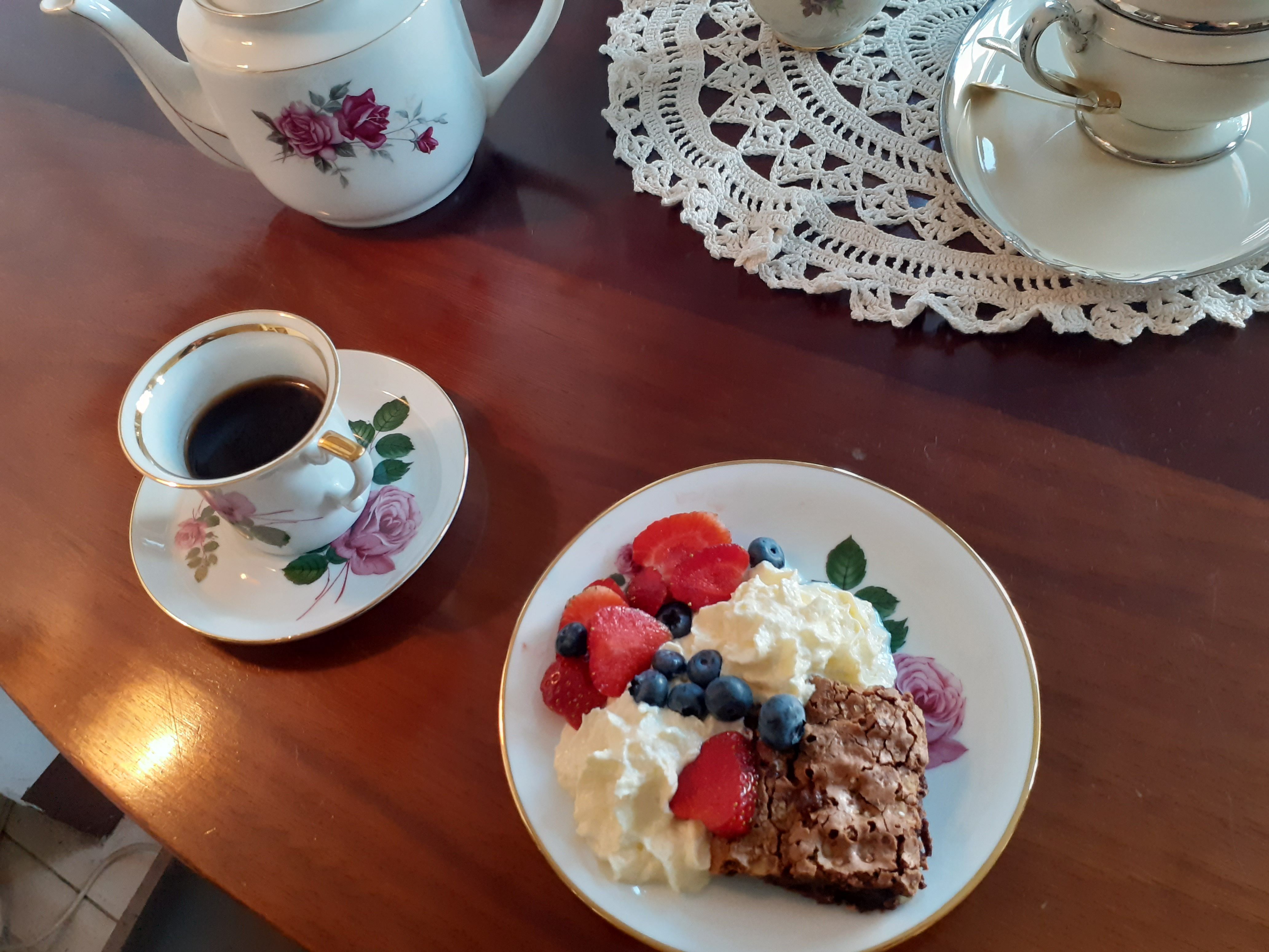 Bord med kaffe, brownie med bær og fløde og to tekopbeholdere med tehætter og blomstermotiver.