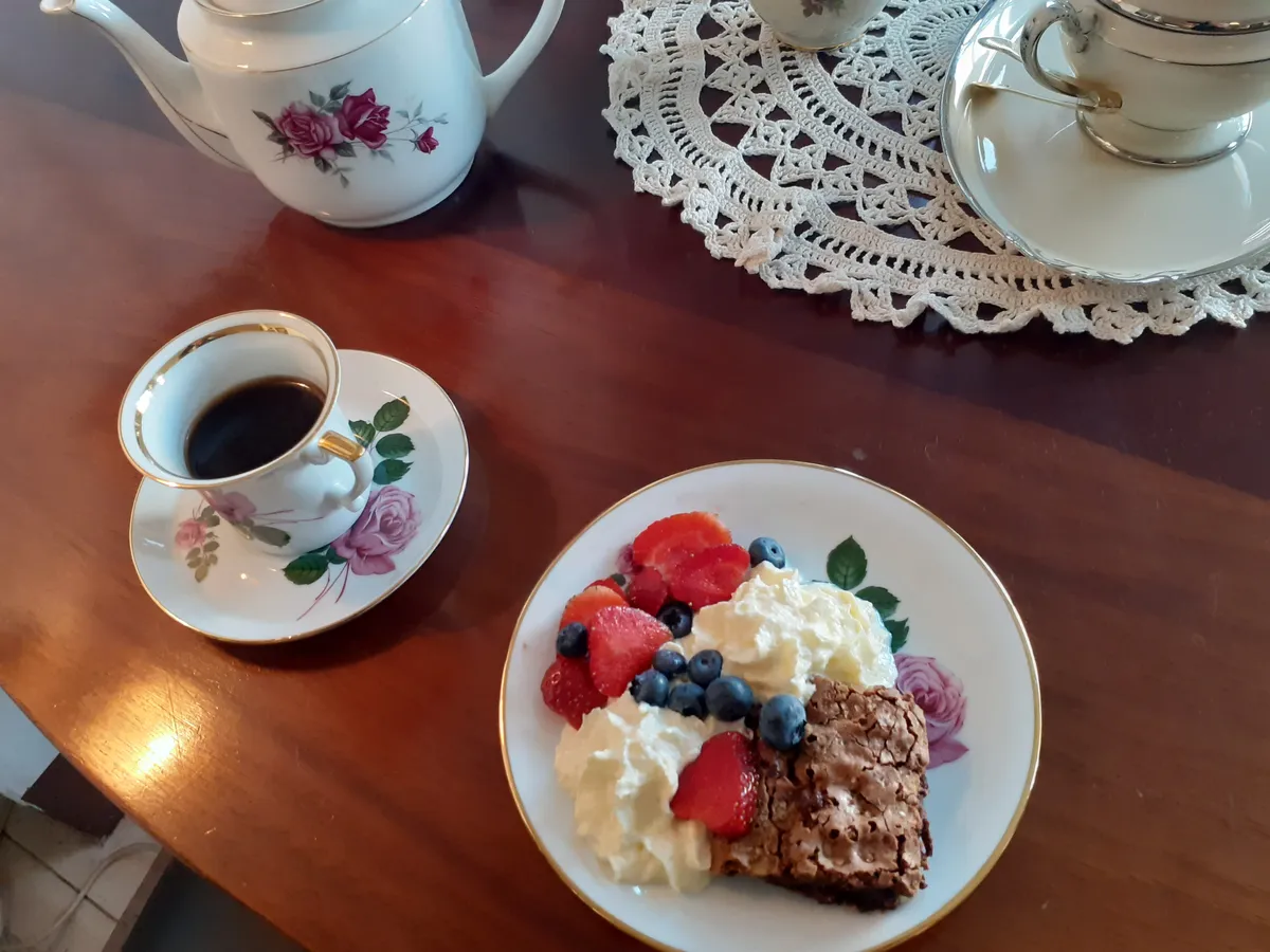 Bord med kaffe, brownie med bær og fløde og to tekopbeholdere med tehætter og blomstermotiver.