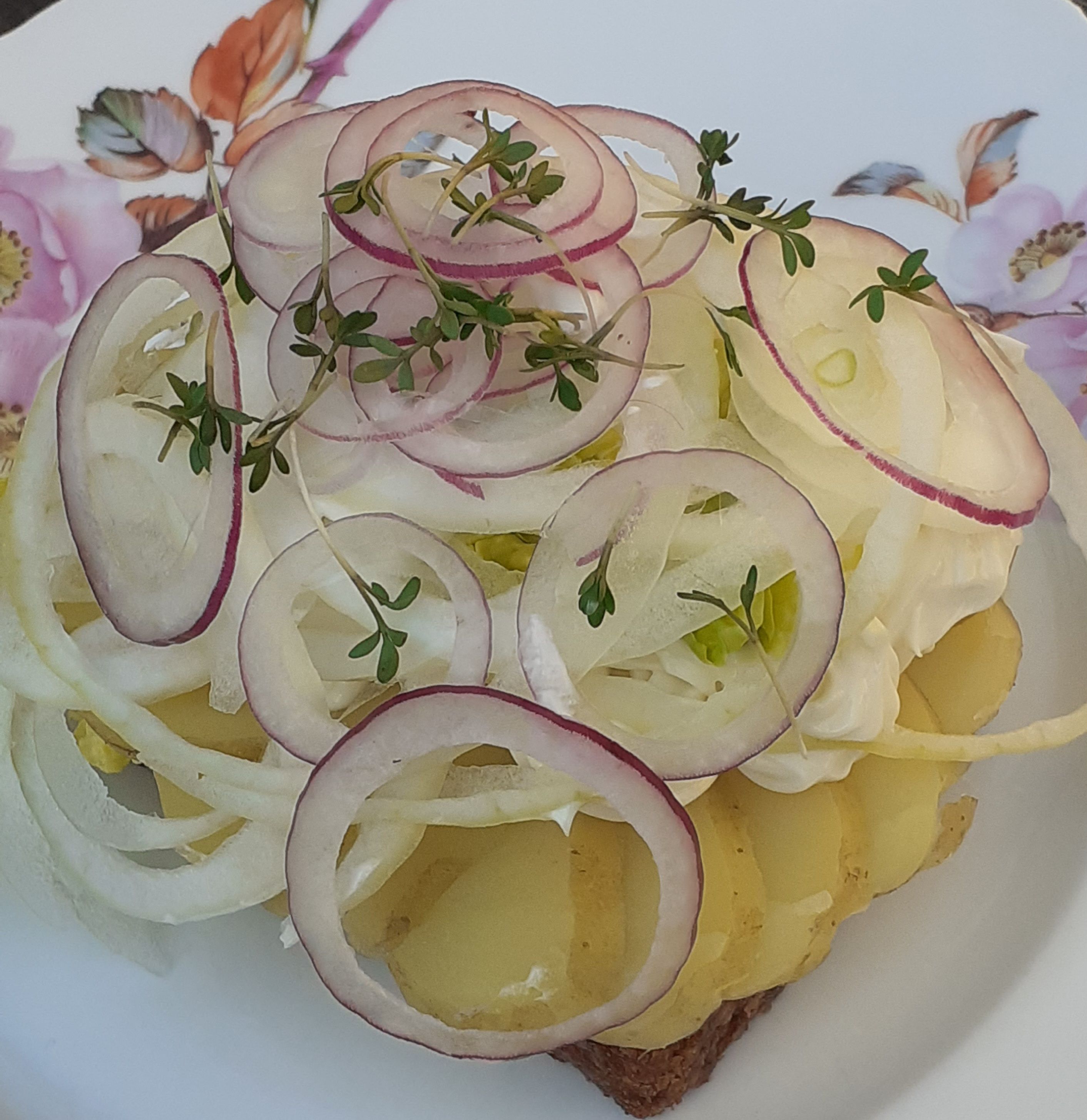 En dansk salat med rødløg, krydderurter og et stykke rugbrød. Salaten serveres på et blomstret serviet med en lækker og